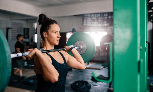 Woman doing squats with barbell in a gym