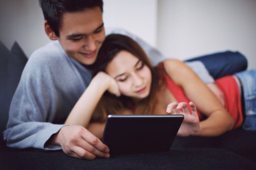Romantic young couple lying on couch using digital tablet