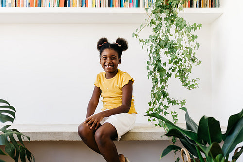 Cheerful afro girl sitting at home, smiling and looking at camera