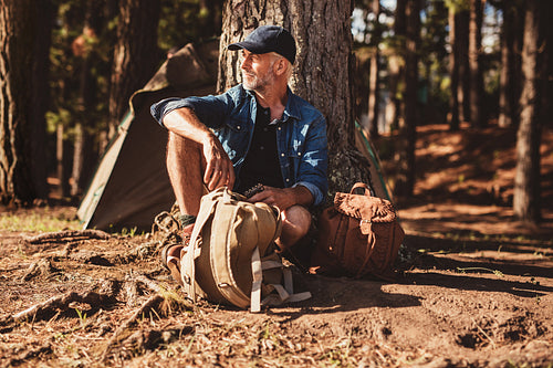 Mature man sitting alone at campsite with backpack