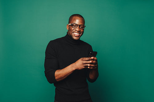 Stylish man holding a mobile phone against a green background