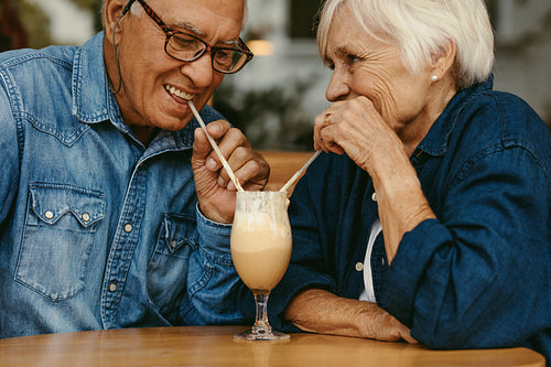 Senior couple in love drinking cold coffee from one glass