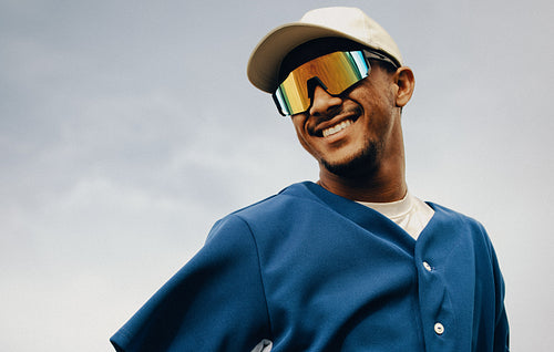 Happy male baseball player wearing polarized glasses smiles confidently under a bright sky