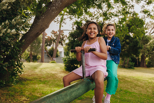Two young children playing on a seesaw in a sunny park setting