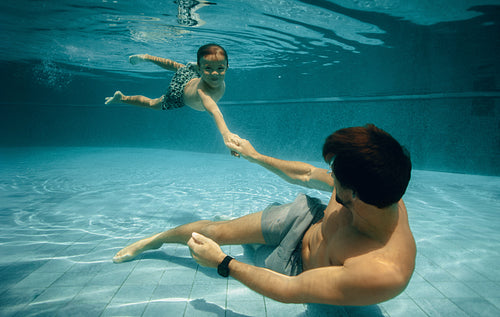 Father and child enjoying underwater swim in pool during holiday