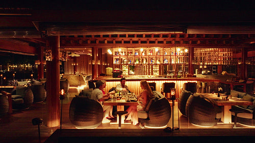 Aerial drone shot of guests enjoying a delicious dinner and toast at a luxurious overwater restaurant at night