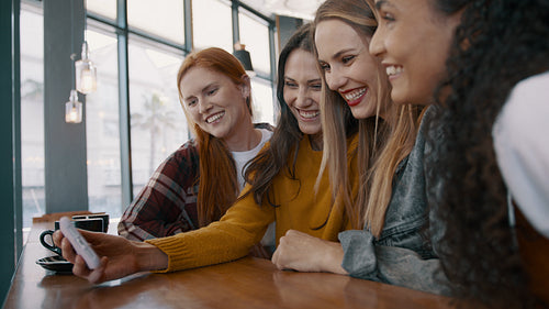 Female friends looking at the phone and smiling at the cafe