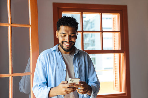 Smiling man using smartphone in a bright room with natural light