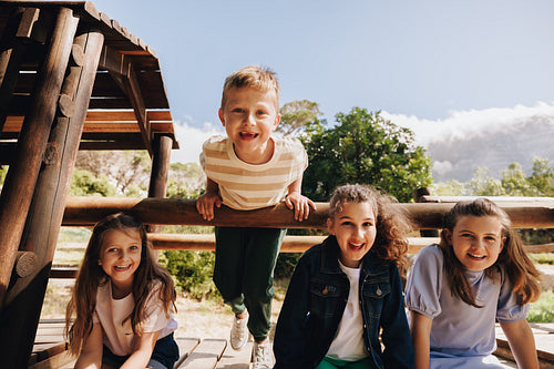 Group of children enjoying outdoor activities at a wooden playground on a sunny day