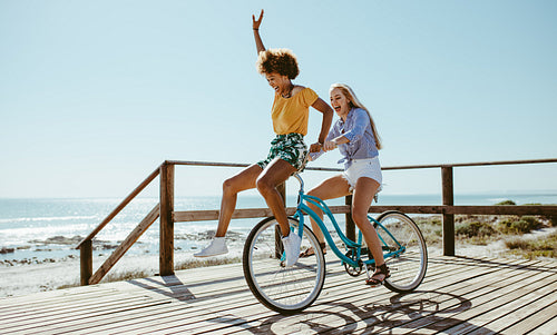 Female friends having fun on a bike at beach