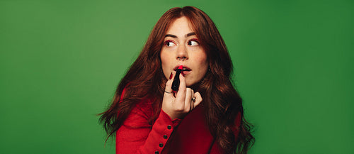 Stylish woman applies vibrant red lipstick in a studio