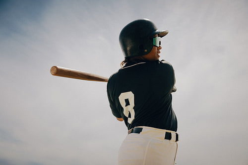 Baseball player in batter's box wearing helmet and attire, preparing to swing the bat on a sunny day.