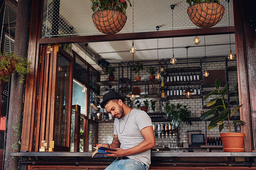 Relaxed young man at cafe counter reading a book