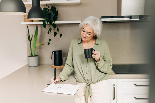 Carefree senior woman writing notes in her diary at home