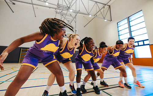 Energetic women basketball team celebrating teamwork at an indoor basketball court