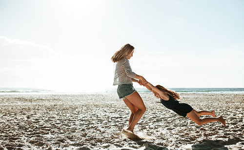 Mother spinning daughter around on the beach