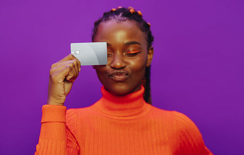 Cheerful woman paying with a contactless card against a vibrant purple background