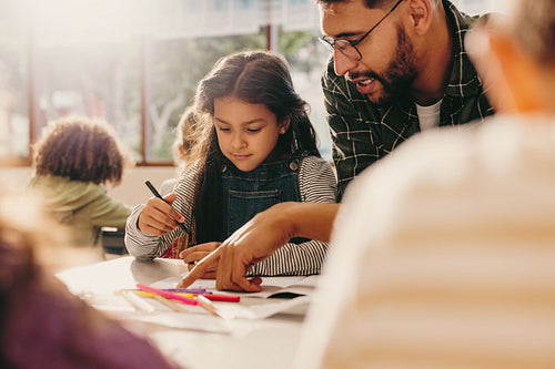 Teacher giving guidance in an art class. Male educator shows a student how to draw