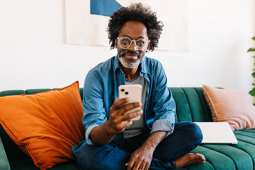 Man with Afro hair sitting on a couch and browsing a mobile app on his phone