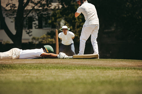 Cricket player diving to make the crease as umpire observes play