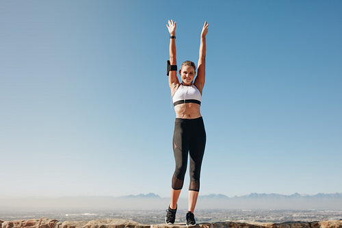 Fitness woman standing on a hill with raised arms