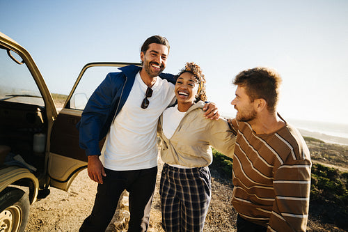 Three friends embrace on a coastal road trip near a vintage van