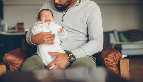 Newborn baby boy crying on his father's lap
