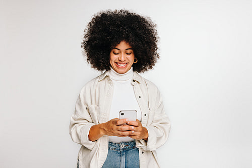Woman with curly hair smiling at her smartphone screen in a studio
