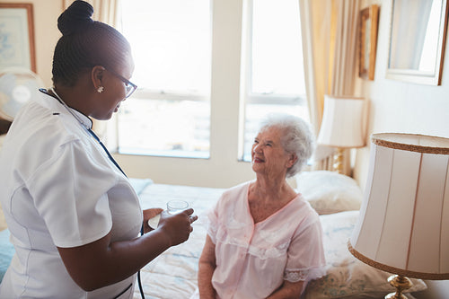 Female nurse giving medicine to senior patient at home