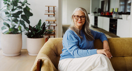 Senior woman sits on a sofa at home
