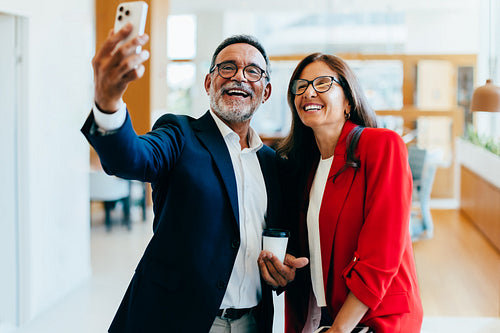 Two senior managers smiling while taking a smartphone selfie together