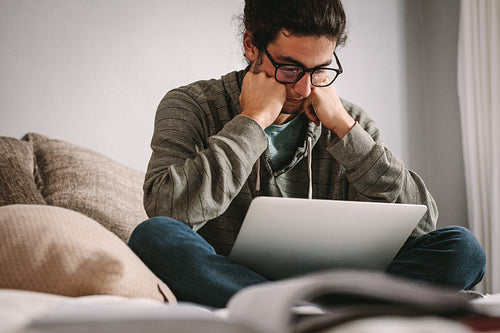 Tensed student looking at laptop sitting at home