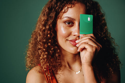Confident woman showcasing green banking card in studio portrait