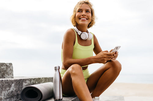 Fit woman smiling and using her smartphone after a yoga workout on the promenade stairs