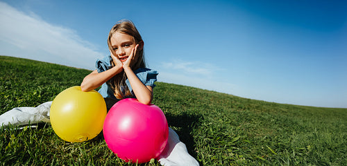 Girl sits on grass with balloons outdoors today