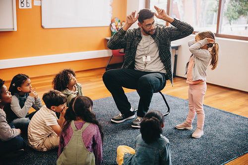Man teaching a primary school class. Teacher shows a little girl how to do heads and shoulders