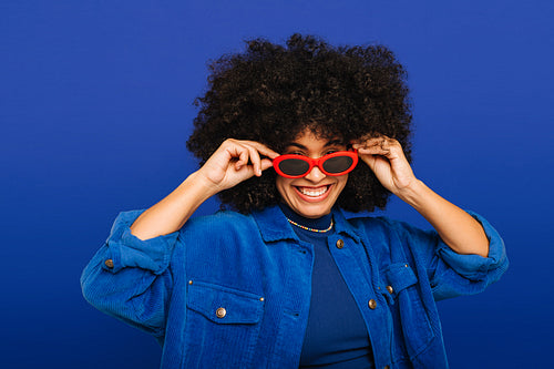 Stylish young woman putting on trendy sunglasses in a studio