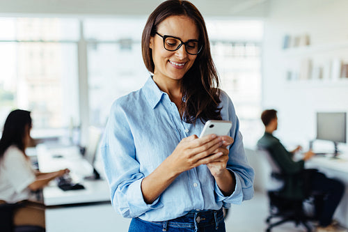 Business woman using a smartphone while standing in an office