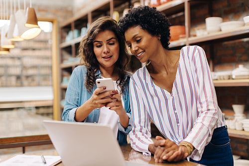 Two female ceramists using a smartphone together in their store