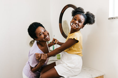 Playful toothbrushing with mom: Young girl smiling with toothpaste in her mouth