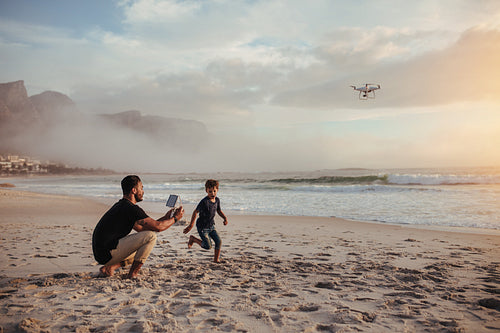 Father and son playing with flying drone on beach