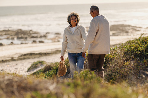 Happy elderly woman pulling her husband by the hand at the beach