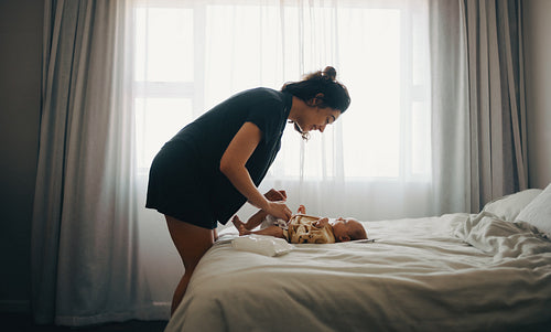 Mother changes baby's diaper on bed