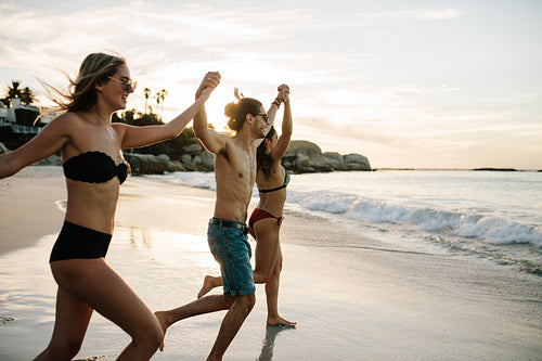 Friends holding hands and running to the sea