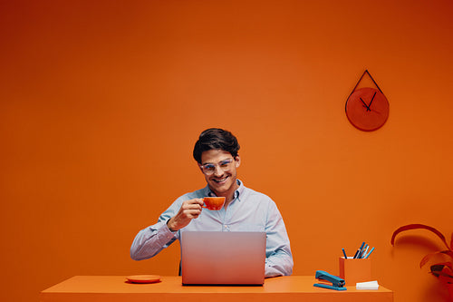 Businessman taking a break with coffee in a monochromatic office while working on a laptop