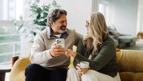 Man points at a smartphone with senior woman at home