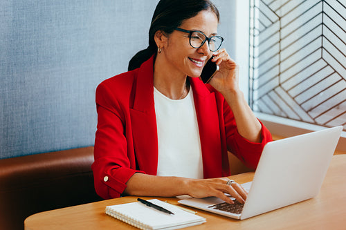 Smiling businesswoman on phone call working on laptop in office environment