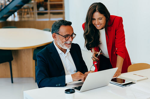 Two senior professionals discussing work at a desk with a laptop