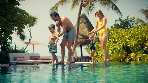 Family with young children on a relaxing tropical vacation entering an infinity pool