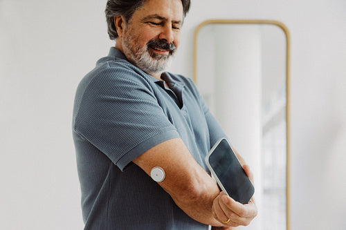 Senior man scans glucose monitor with smartphone at home